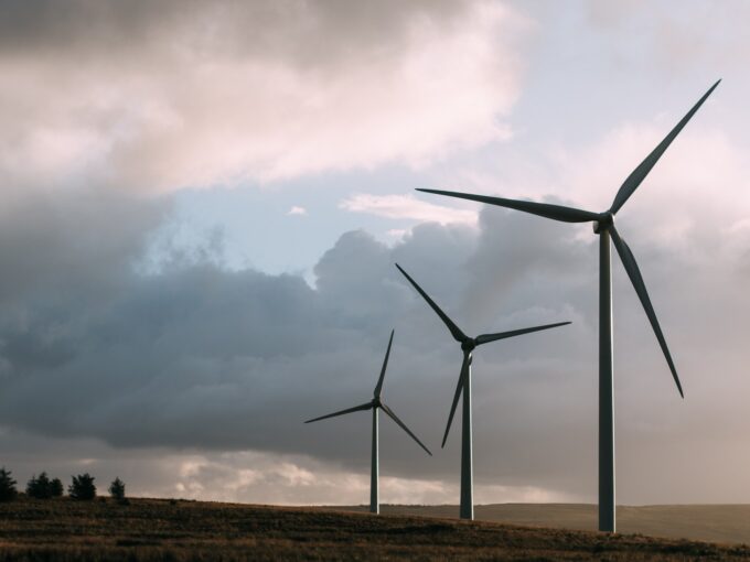 Three tall wind turbines stand on a grassy hillside under a cloudy sky, contributing to renewable energy generation.